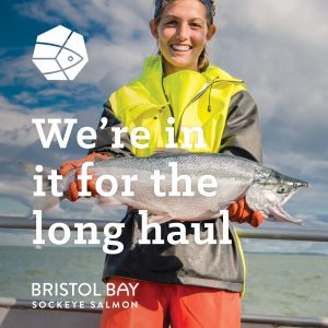 A female fisherman wearing brightly colored gear holding a whole sockeye salmon with the text "We're in it for the long haul" overlaid.