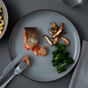 A gray tabletop with a gray plate of crispy skin salmon, mushrooms and kale.