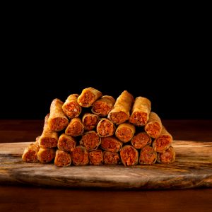 A stack of sockeye salmon lumpia on a long wooden platter against a black background.