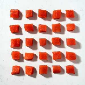 Cubes of uncooked sockeye salmon arranged in a grid on a white marbled surface.