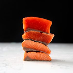 A stack of sockeye salmon portions, each showing different levels of doneness from uncooked to fully cooked.