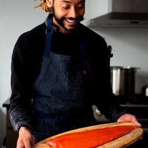 A chef holding a wooden platter with an uncooked sockeye salmon fillet.