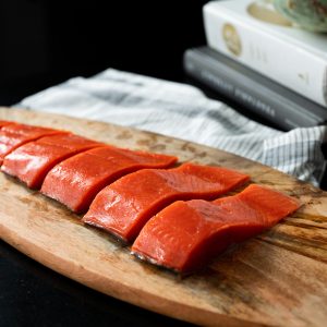 A wooden platter with a sliced uncooked sockeye salmon fillet.