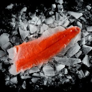 A frozen sockeye salmon fillet surrounded by chunks of ice on a black surface.