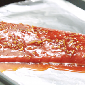 A close up of an uncooked sockeye salmon fillet coated in a glaze on a foil-lined sheet pan.