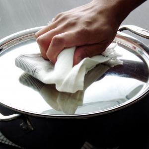 Video still of a hand placing the lid on a stainless steel pan using a cloth napkin as a potholder.