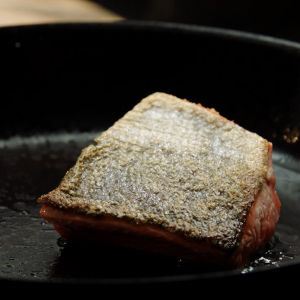 A cast iron skillet on a gas stove with a crispy skin sockeye salmon portion sizzling in the center.