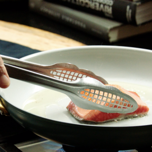 A pair of tongs grabbing a sockeye salmon fillet from a pan.