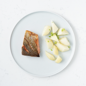 A white plate with a crispy skin sockeye fillet next to peeled potatoes sprinkled with scallions.