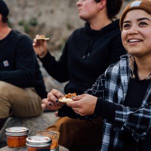 A group of people sitting on a beach enjoying jarred salmon on crackers.