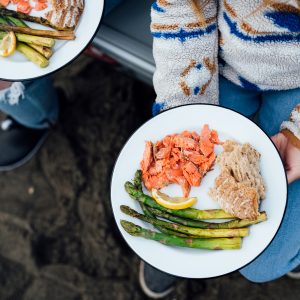 Bird's eye shot of a woman holding a white plate with salmon, asparagus and bread.