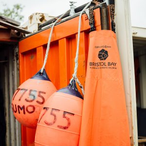 The open door of an orange shipping container with two orange buoys hanging down and an orange rubber apron hanging on the edge.