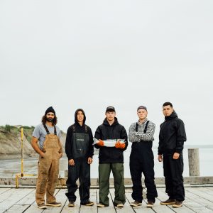 A group of five fishermen standing on a dock, the man in the center holding a whole sockeye salmon.