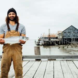 A fisherman holding a whole sockeye salmon on a dock.