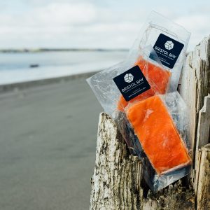 Two packages of Bristol Bay Sockeye Salmon resting on a weathered wooden post on a beach.