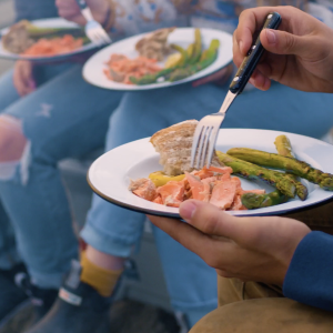 Close up of people holding white plates with salmon, veggies and crusty bread.