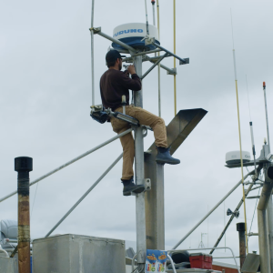 A fisherman doing repairs to a pole on a fishing boat.