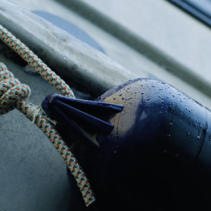 Close up of a blue float on the side of a boat secured with rope.