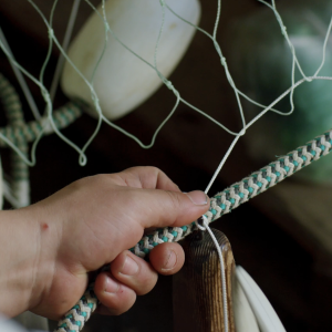Close up of a fishing net and a hand mending it.